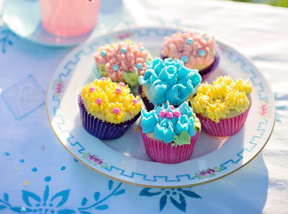 A plate of cupcakes decorated with rosebuds in blue, yellow, and pink.