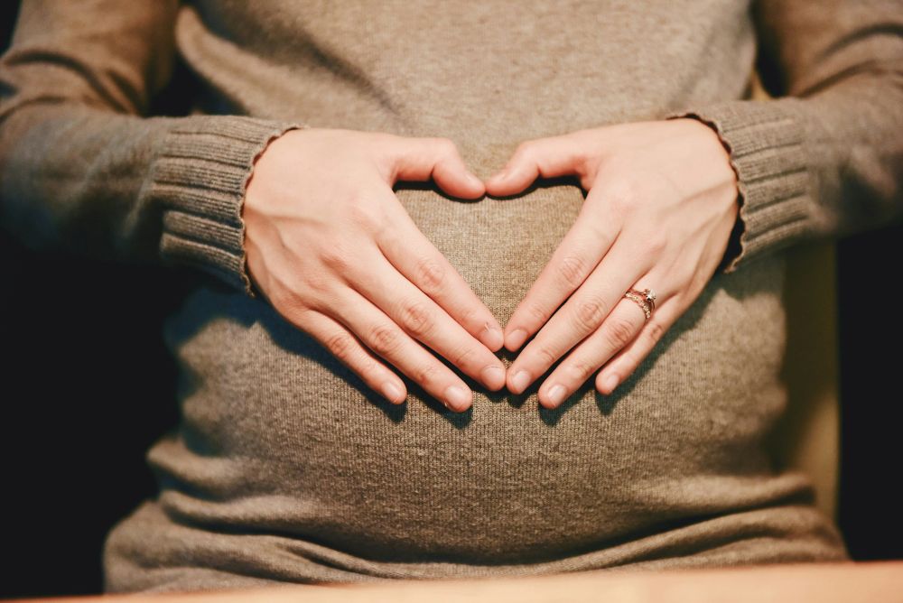 Woman holding her pregnant belly with her hands in the shape of a heart