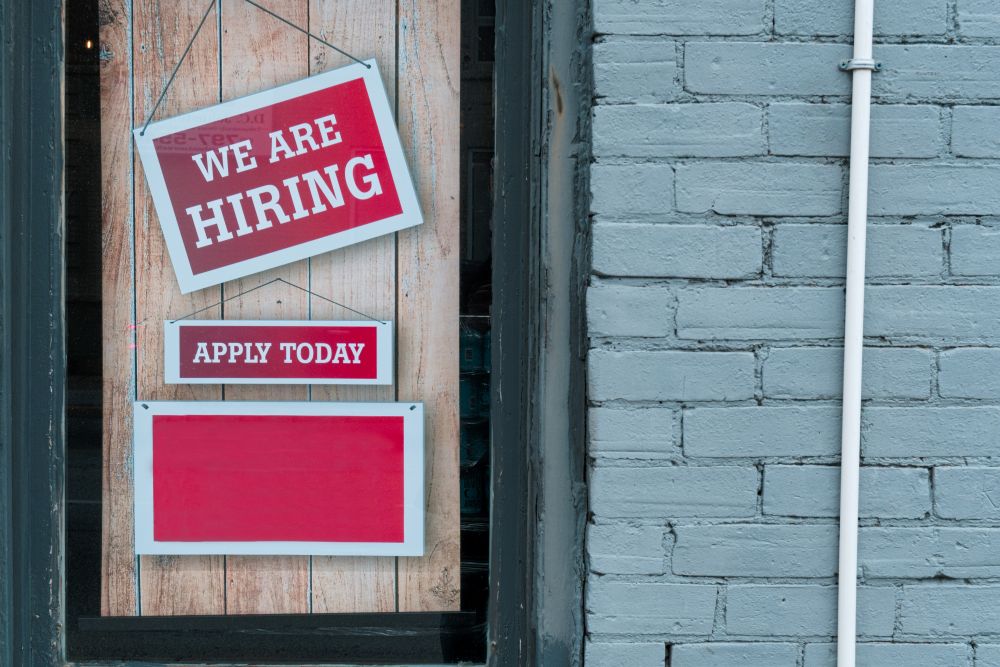 Closed shop door with signs reading "We are Hiring" and "Apply Today"