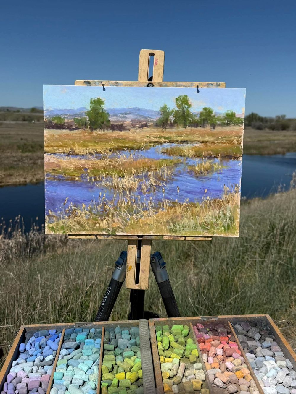 Easel with landscape painting aligned with background landscape so that the painting blends into the surrounding environment.